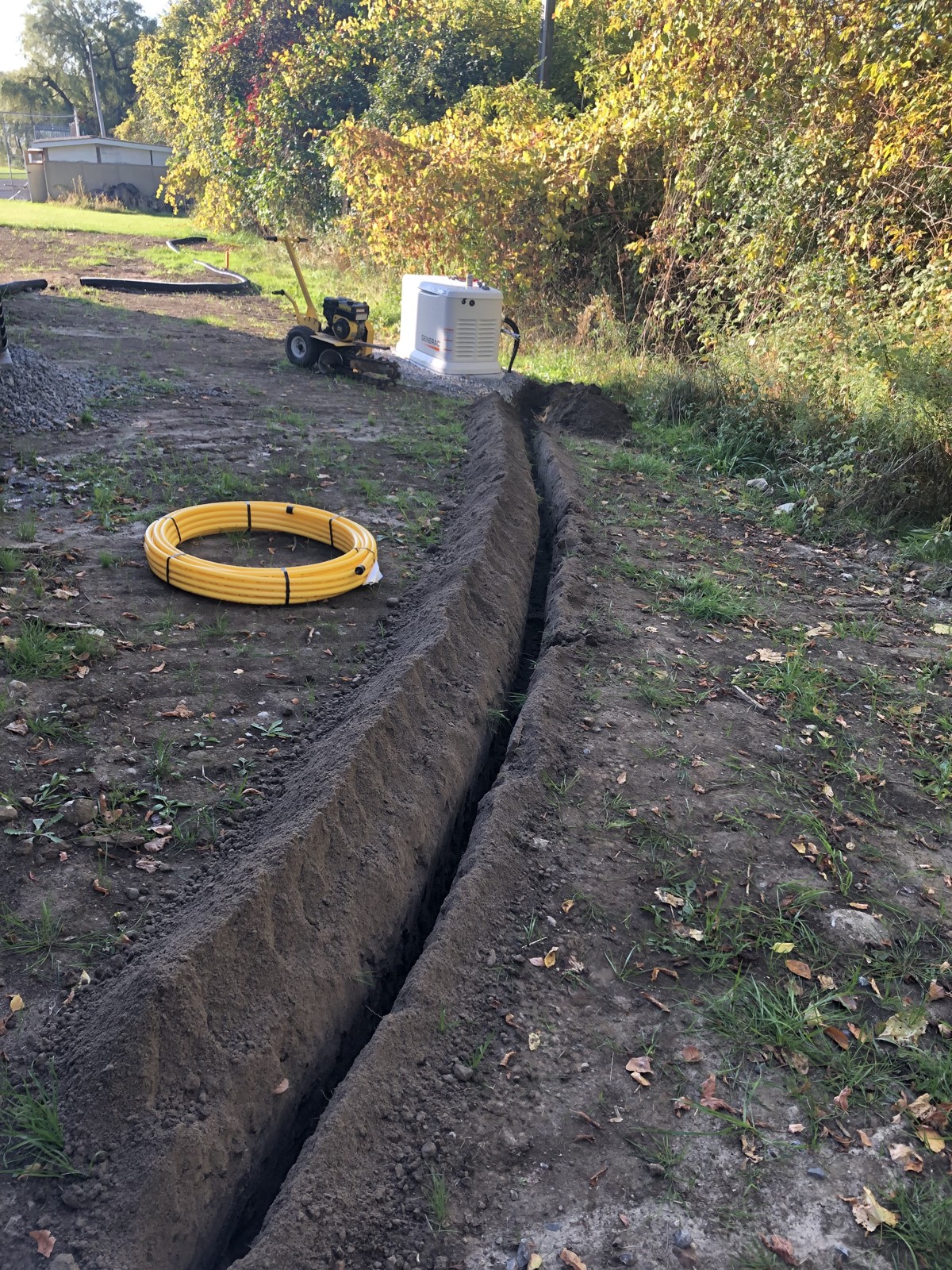 Underground gas-line trench with yellow piping, trencher and standby generator